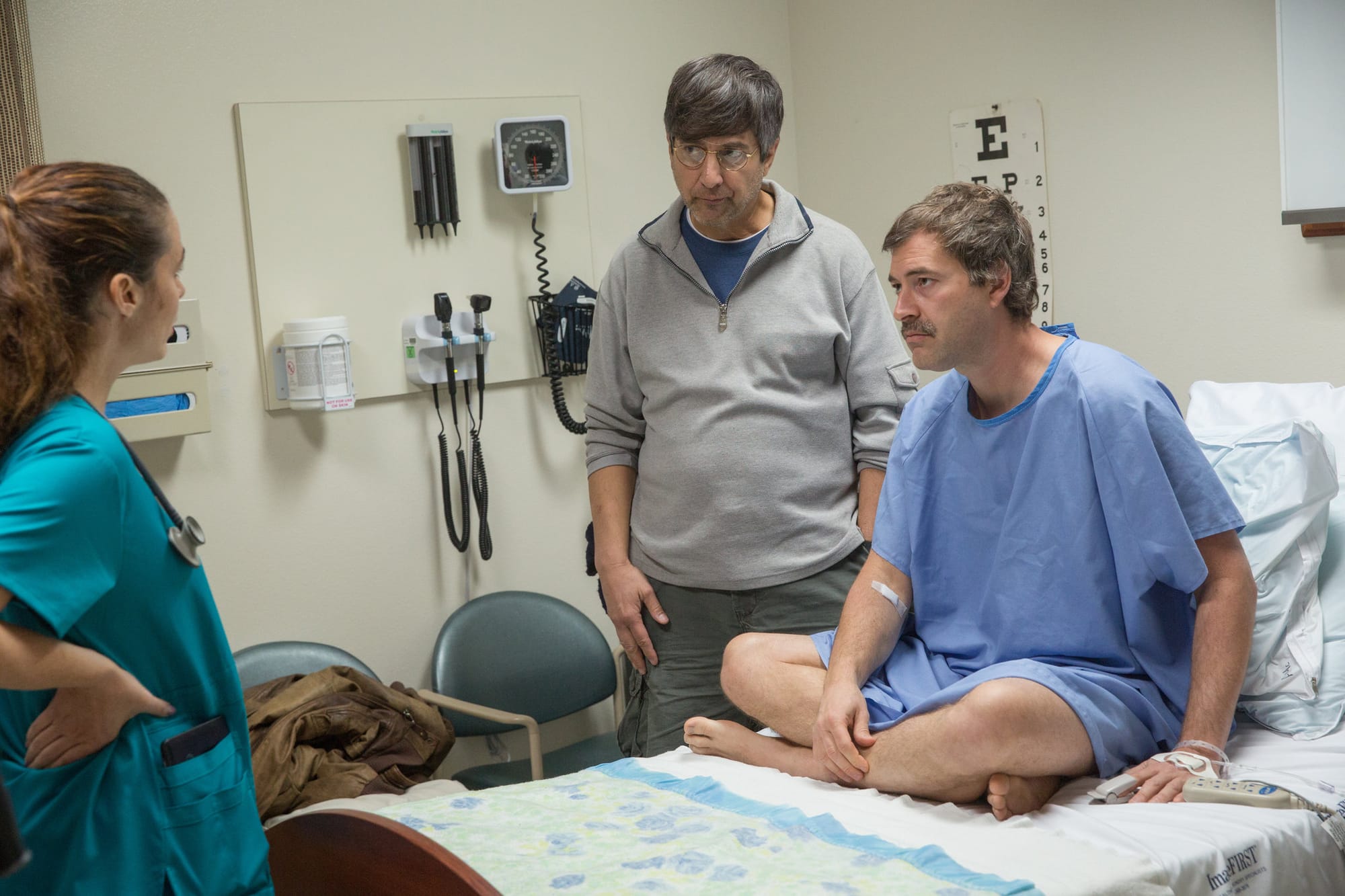 Michael in a hospital bed with Andy stood beside him, listening to the nurse.