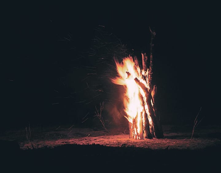 Image of a large bundle of upright sticks, on fire at night.