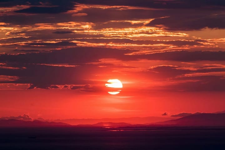 A red-tinted sky at sunset. Dark foreground and dark clouds streaking overhead.